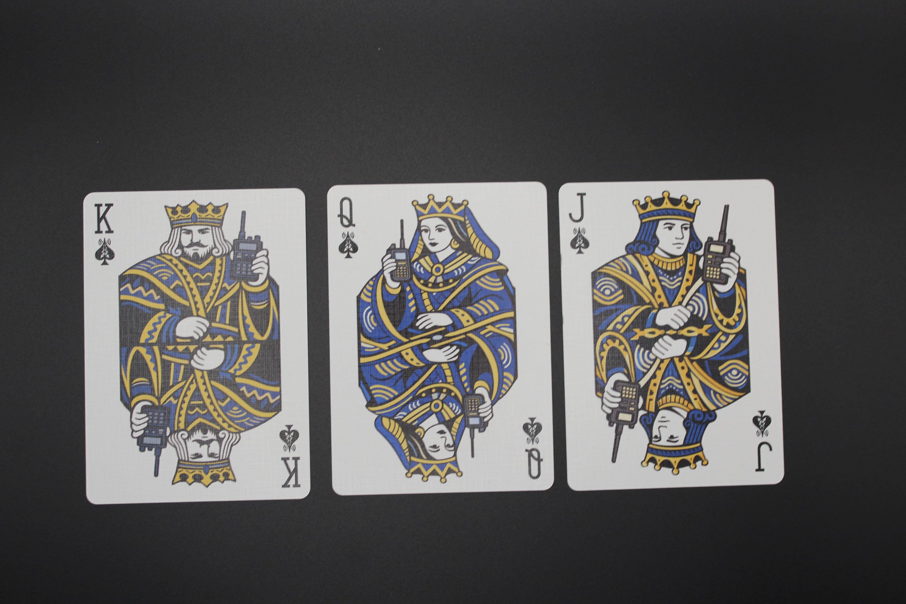 Three playing cards featuring a king, queen, and jack with unique designs on a black background.