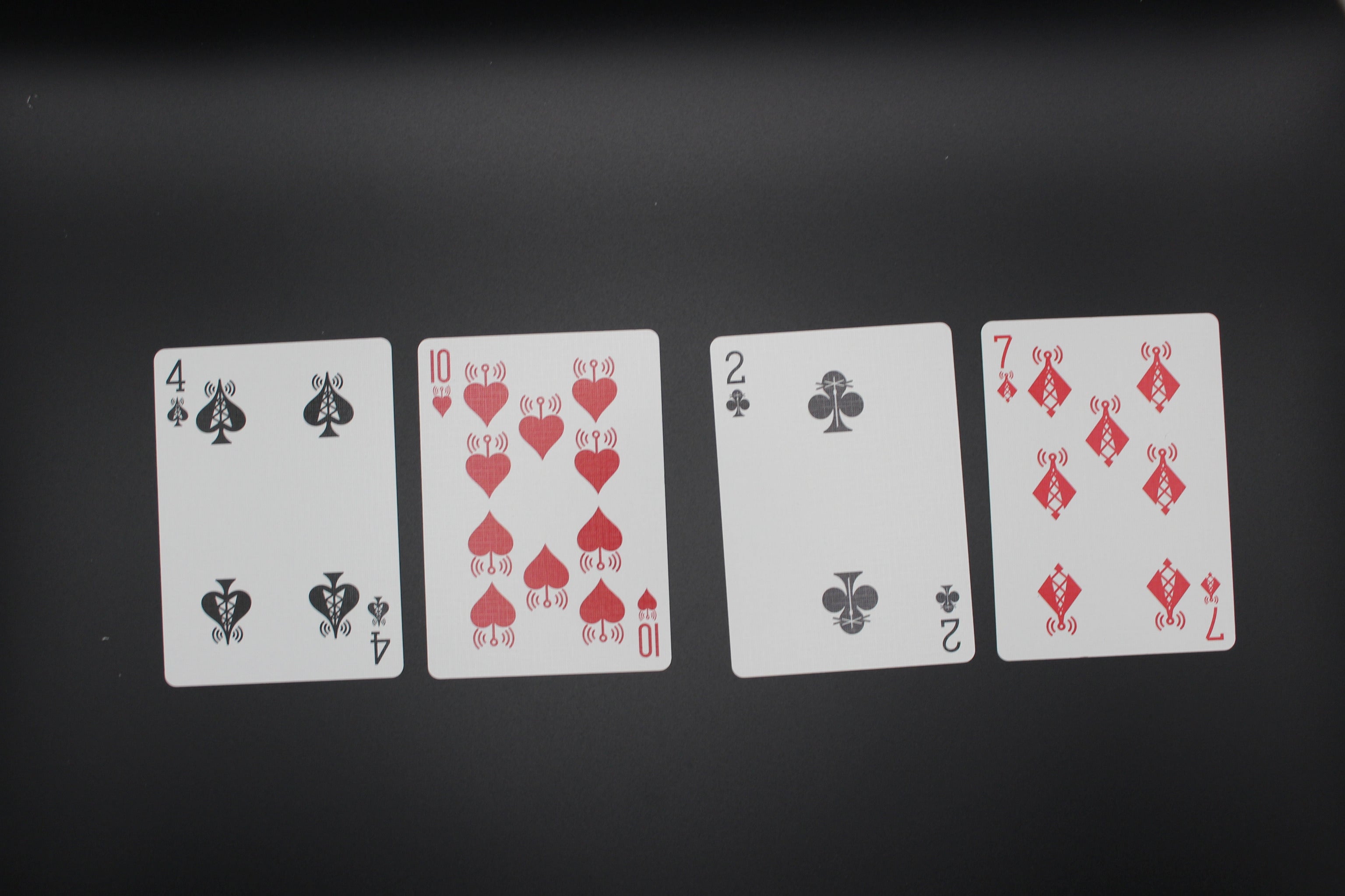 Four playing cards (4 of spades, 10 of hearts, 2 of clubs, 7 of diamonds) arranged on a black background.